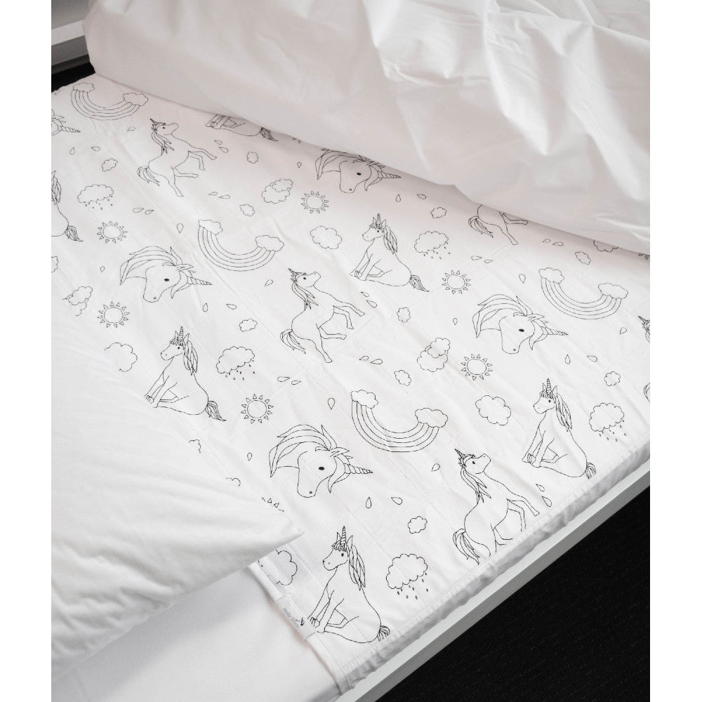 A white quilted brolly sheet mattress protector with a black line-art unicorn and rainbow pattern, shown partially pulled down over a bed with white bedding.