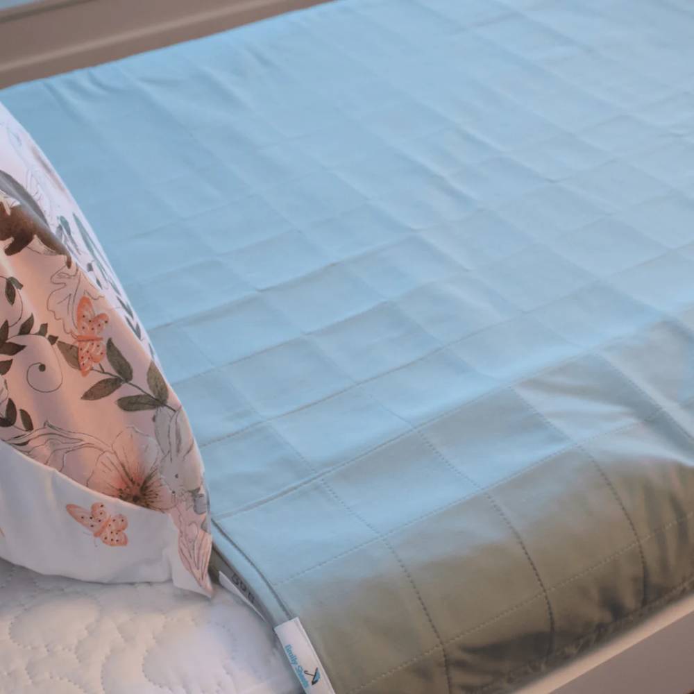 A light green quilted mattress brolly sheet laid over a white mattress, with a floral-patterned pillow partially visible on the left.