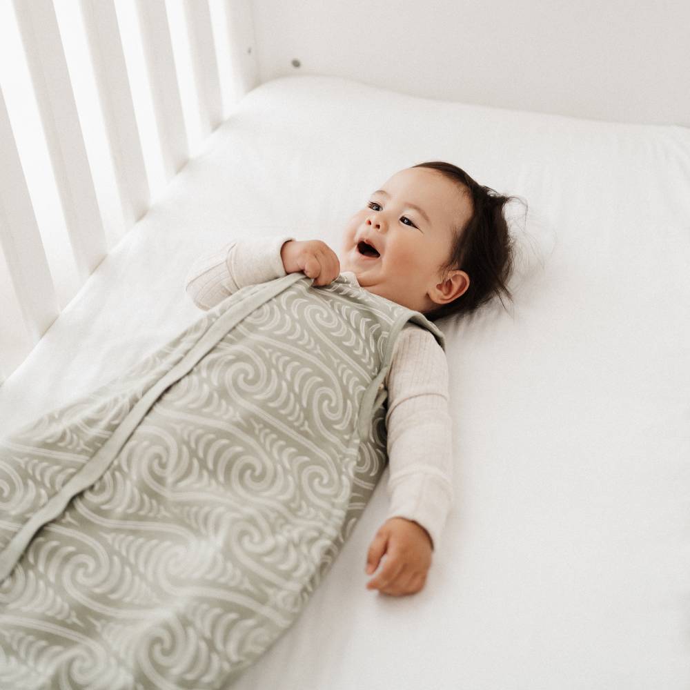 Yawning Baby lying in a crib with a patterned green sleeping bag