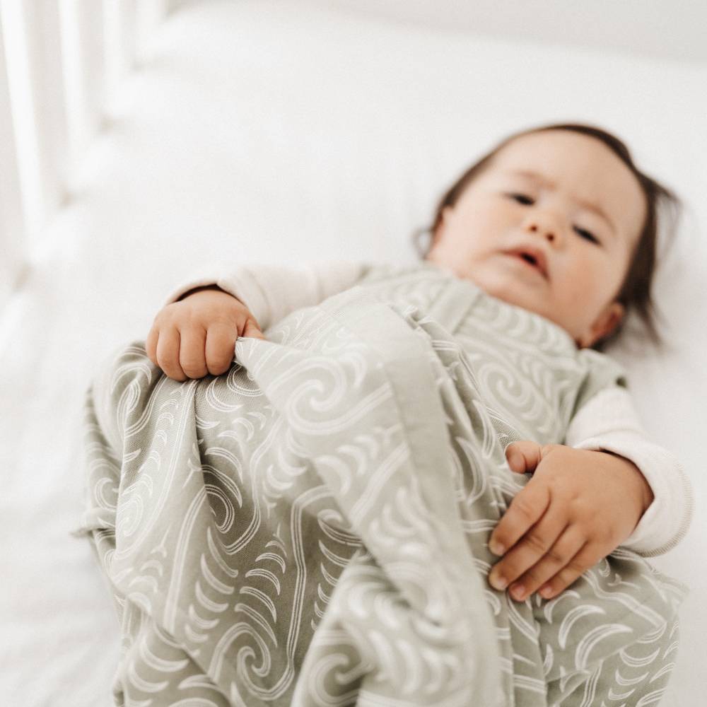 Baby wrapped in a patterned wearable blanket on a white bed