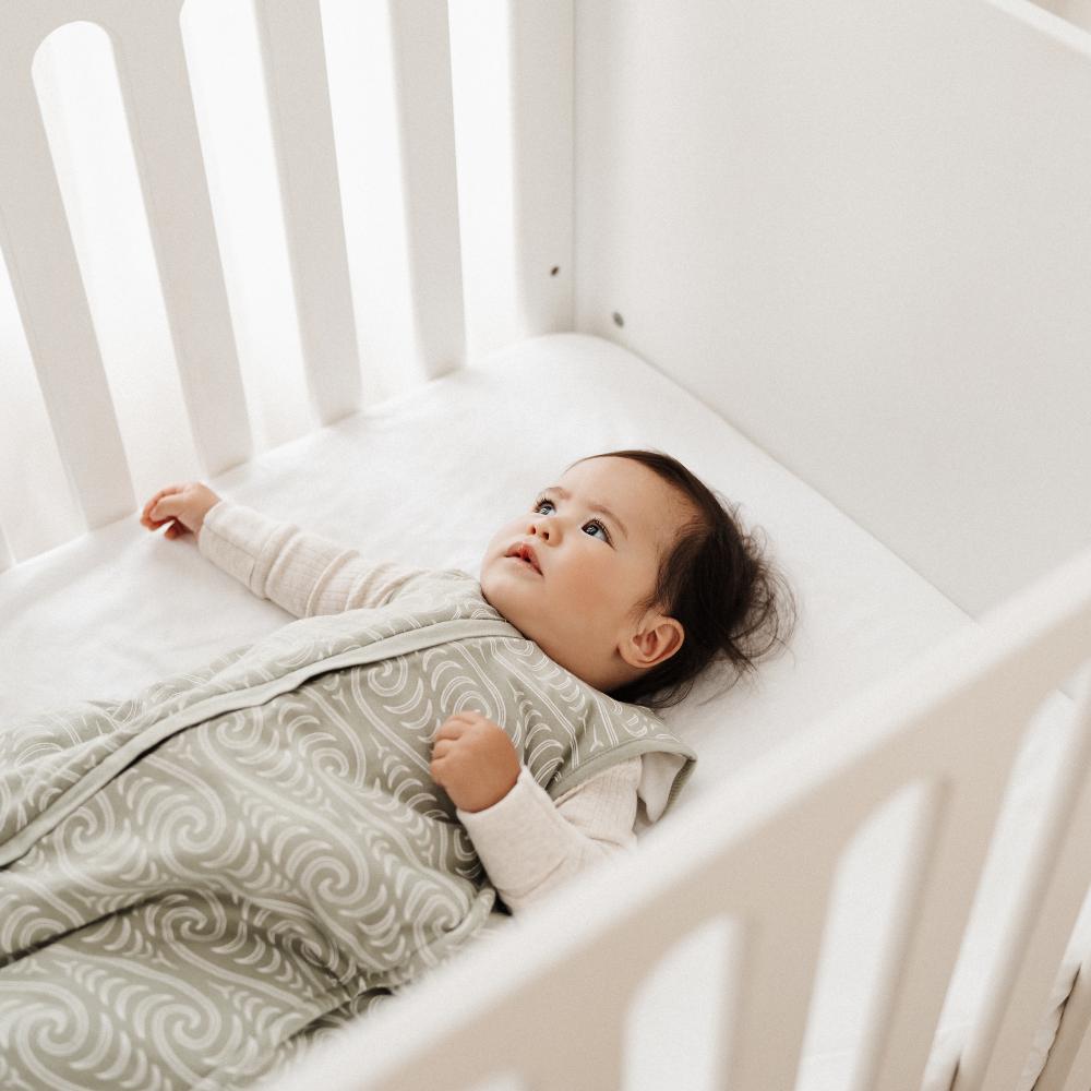 Baby lying in a crib with a white and gray patterned blanket
