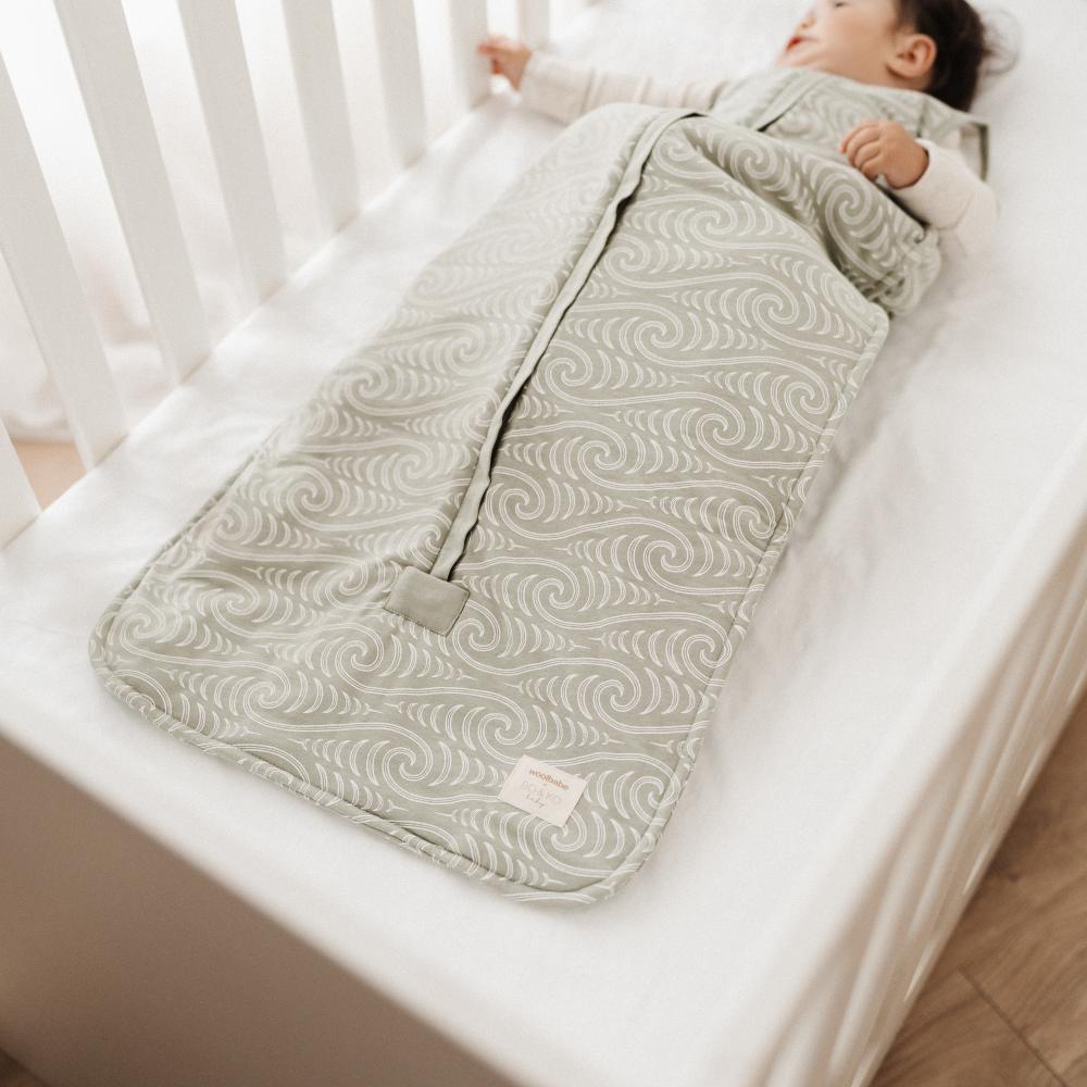 Baby sleeping in a crib with a green patterned sleeping bag
