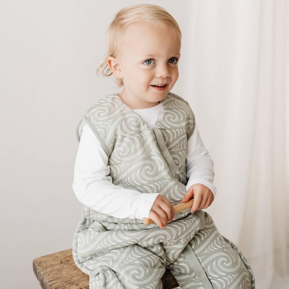 Child wearing a patterned outfit sitting on a wooden stool against a plain background