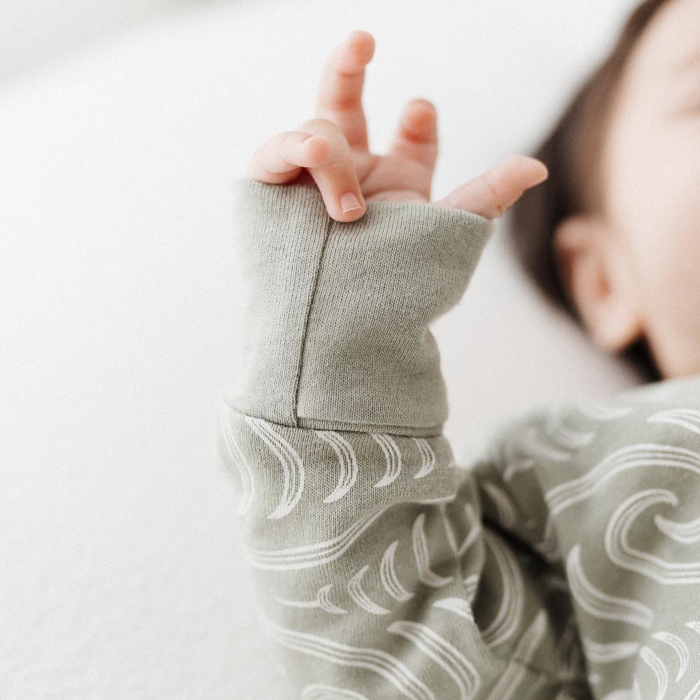 Close-up of a child's hand wearing a gray sleeve with a subtle Maori pattern on a light background