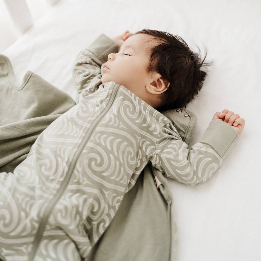 Baby lying on a white surface wearing a Maori patterned onesie