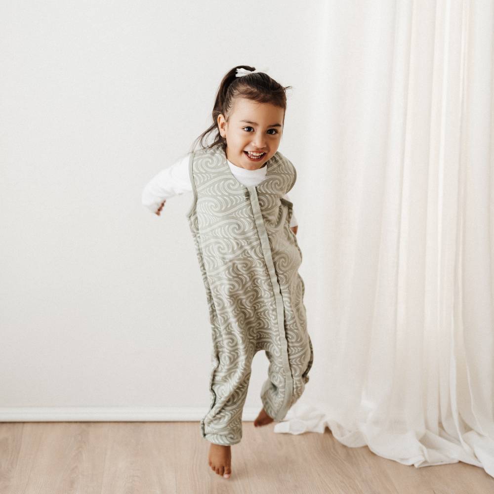 Child wearing a Bo + Ko Maori patterned onesie standing in a room with white walls and curtains.