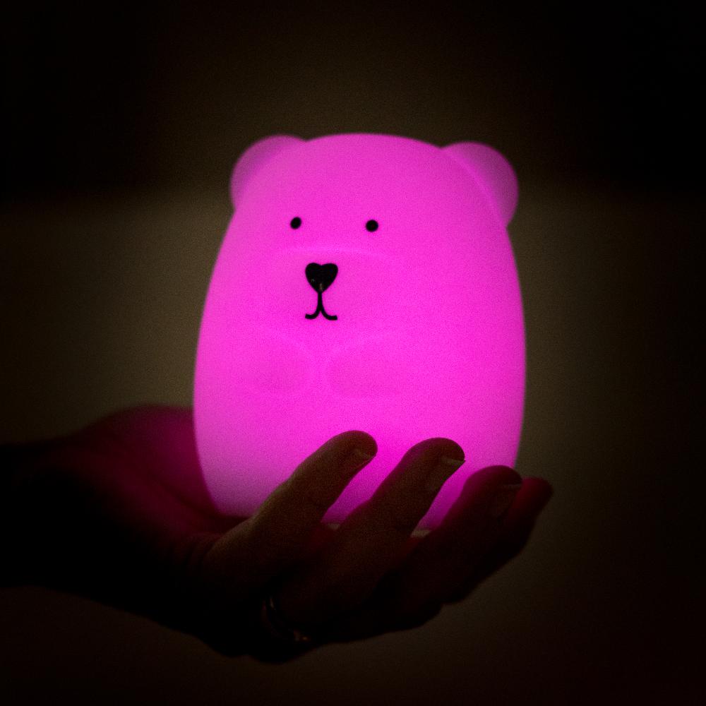 Pink bear-shaped night light held in a hand against a dark background