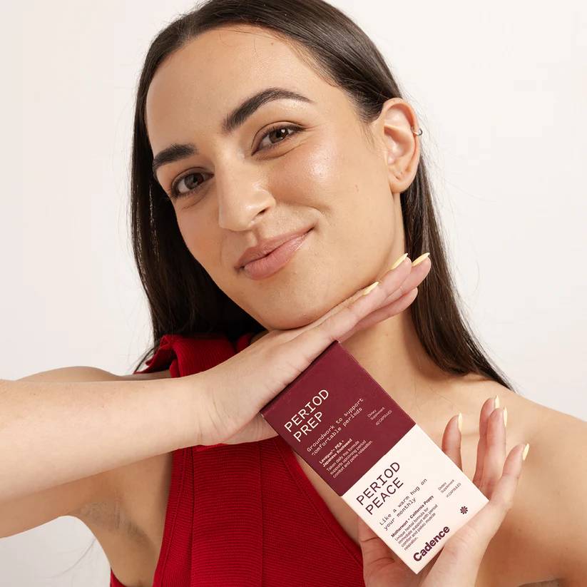 A woman in a red top holds a box of Period Prep/Period Peace against a clean white background.