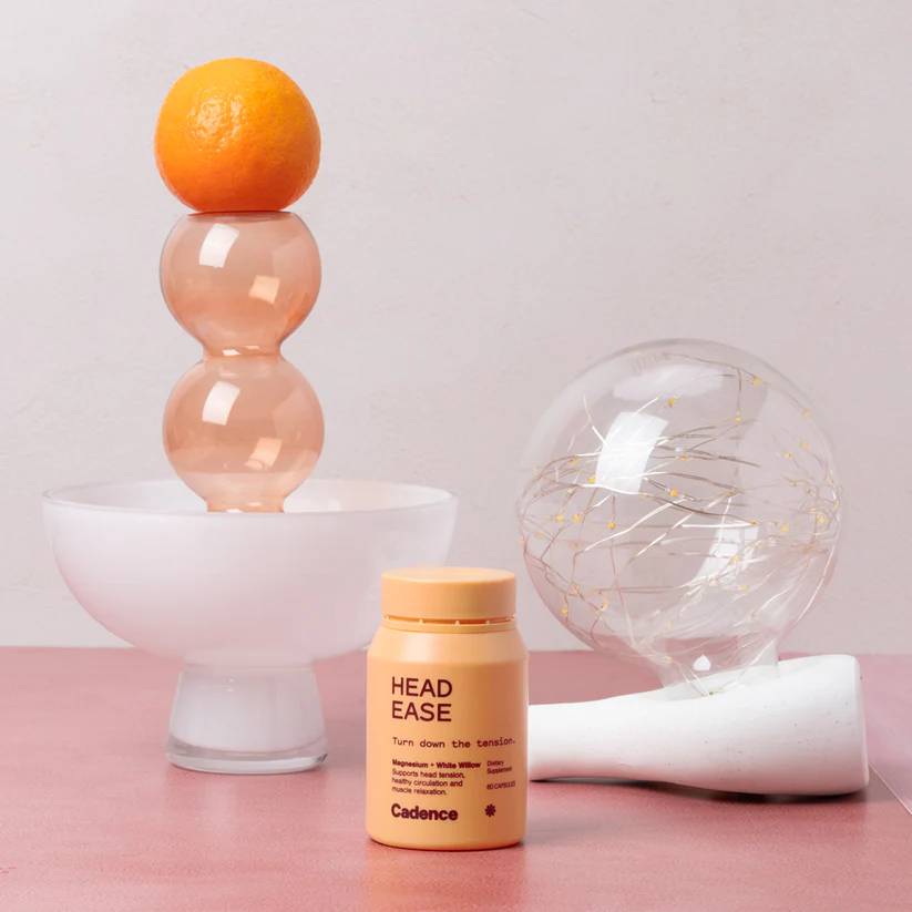 Orange on a stand with a bottle labeled 'HEAD EASE' and decorative items on a pink surface.