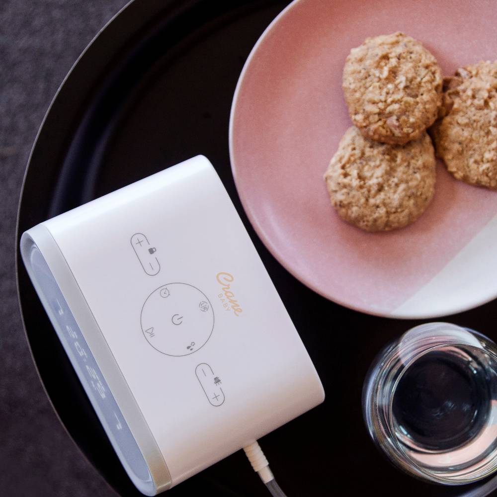 Double electric breast pump on a dark surface with a pink plate of cookies and a glass container.