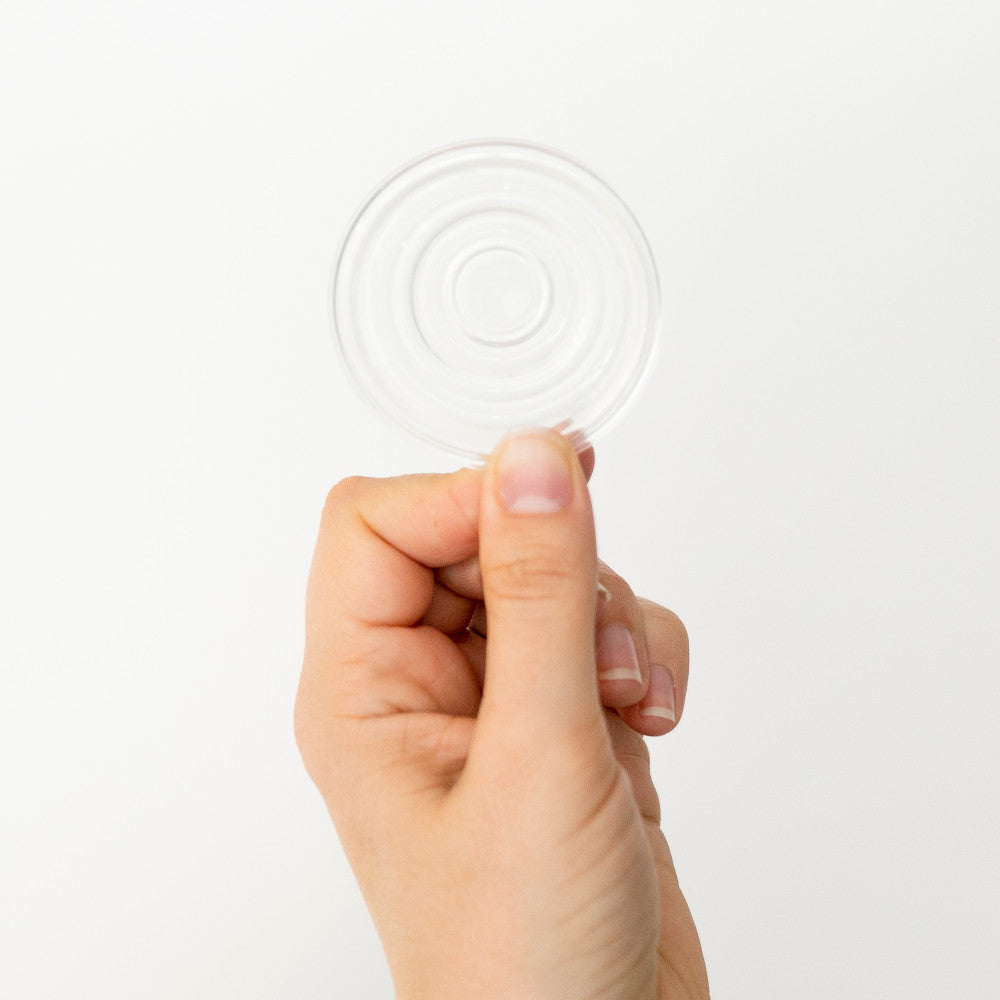 A hand holding a clear circular plastic diaphram against a plain white background.