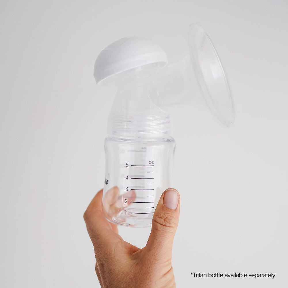 A hand holding a clear breast pump bottle with a white flange and transparent silicone pump head, shown against a light gray background. Measurement markings are visible on the bottle.