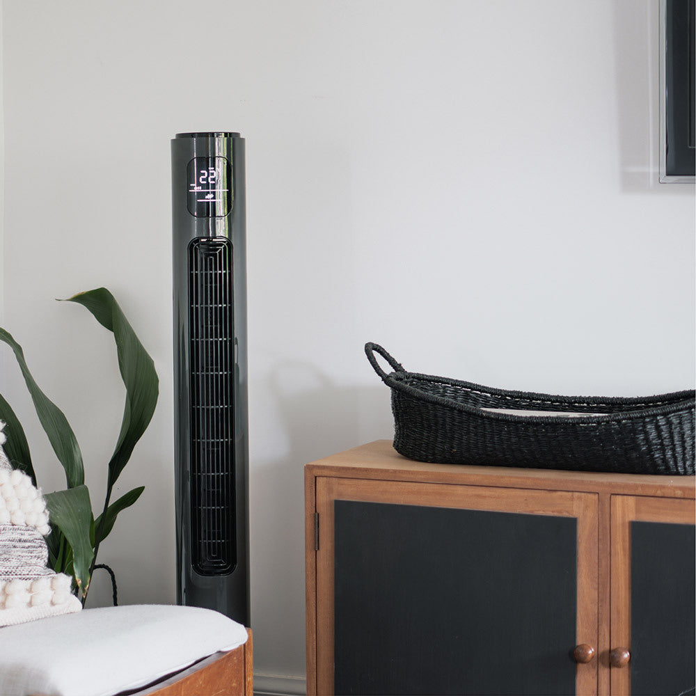 Tall charcoal tower fan in a room with a wooden cabinet and plant.