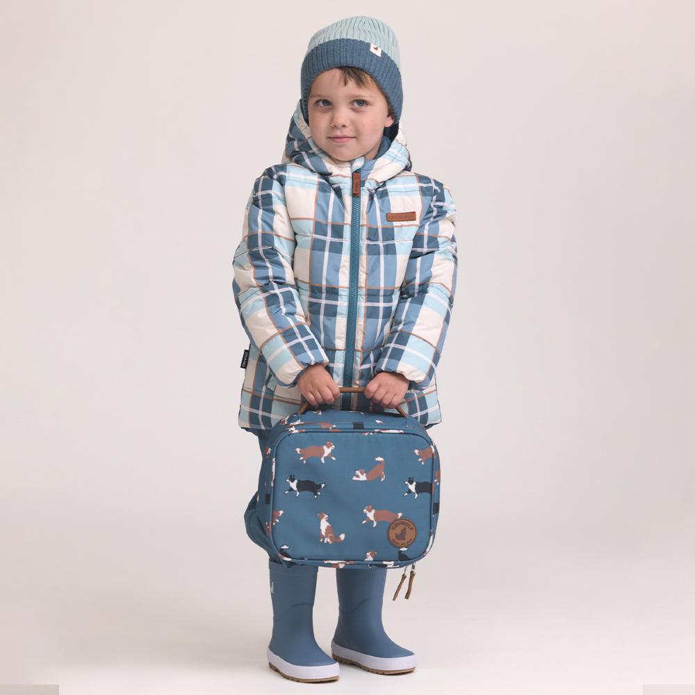 Child wearing a plaid jacket and holding a blue lunch bag with dog illustrations on a plain background