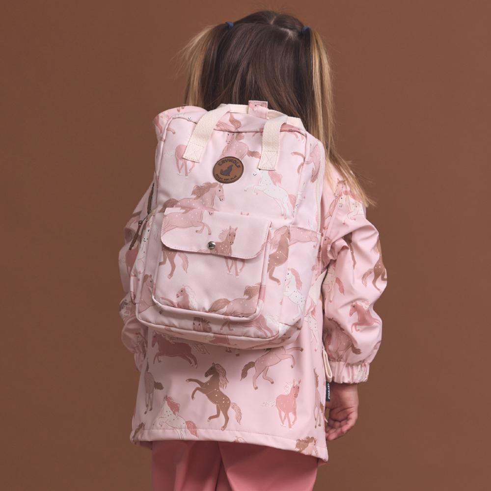 Child wearing a pink jacket with horse patterns and a matching backpack on a brown background