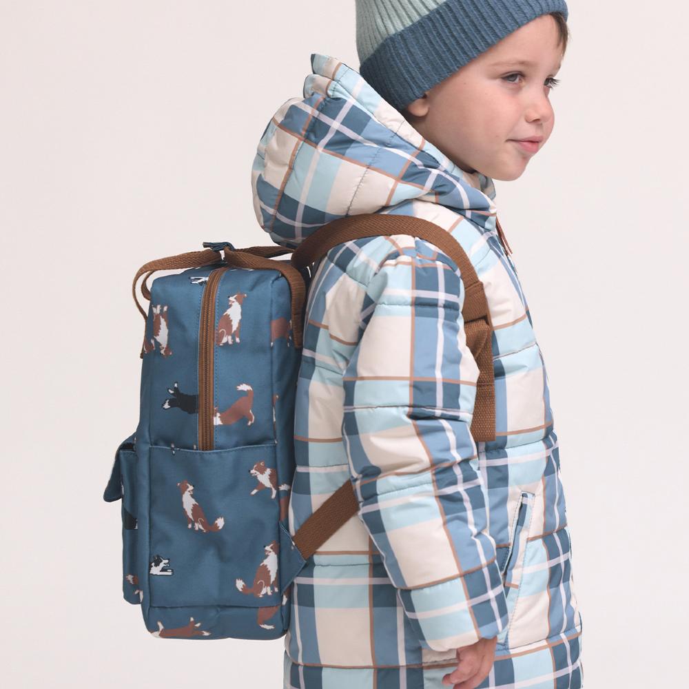 Child wearing a blue plaid coat with a patterned backpack on a light background