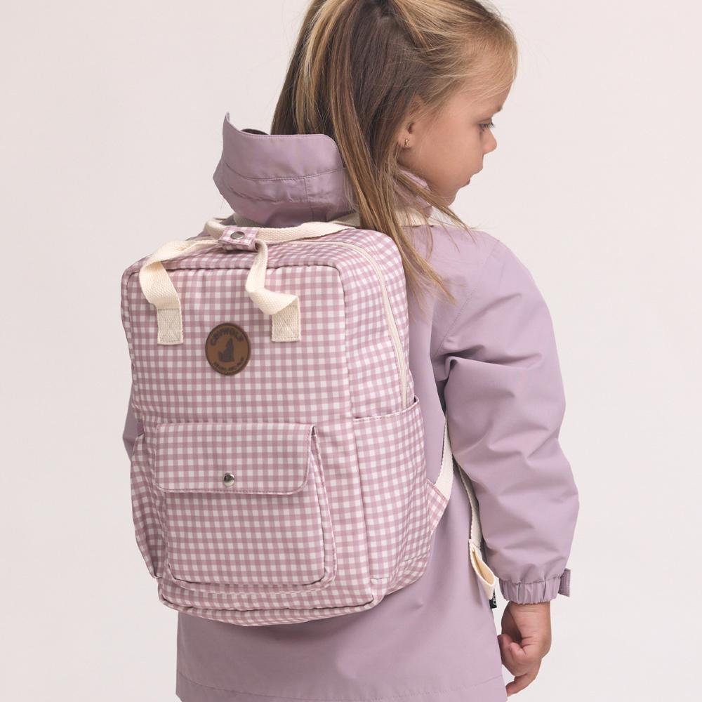 A young girl wearing a lavender hooded jacket and carrying a pink and white gingham backpack, shown from a side-back angle against a plain light background.