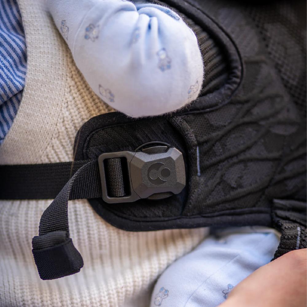 Close-up of a baby's foot in a blue sock with a black magnetic baby carrier buckle