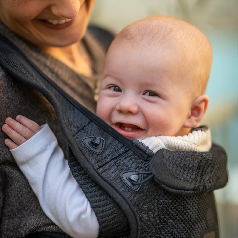 Baby in a carrier smiling outdoors with a blurred background