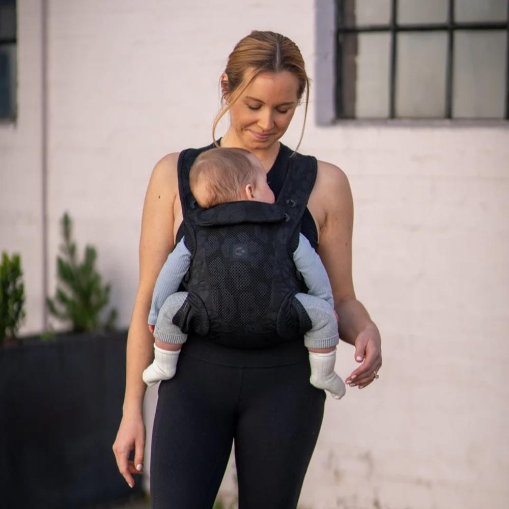 Woman carrying a baby in a black baby carrier against a neutral background