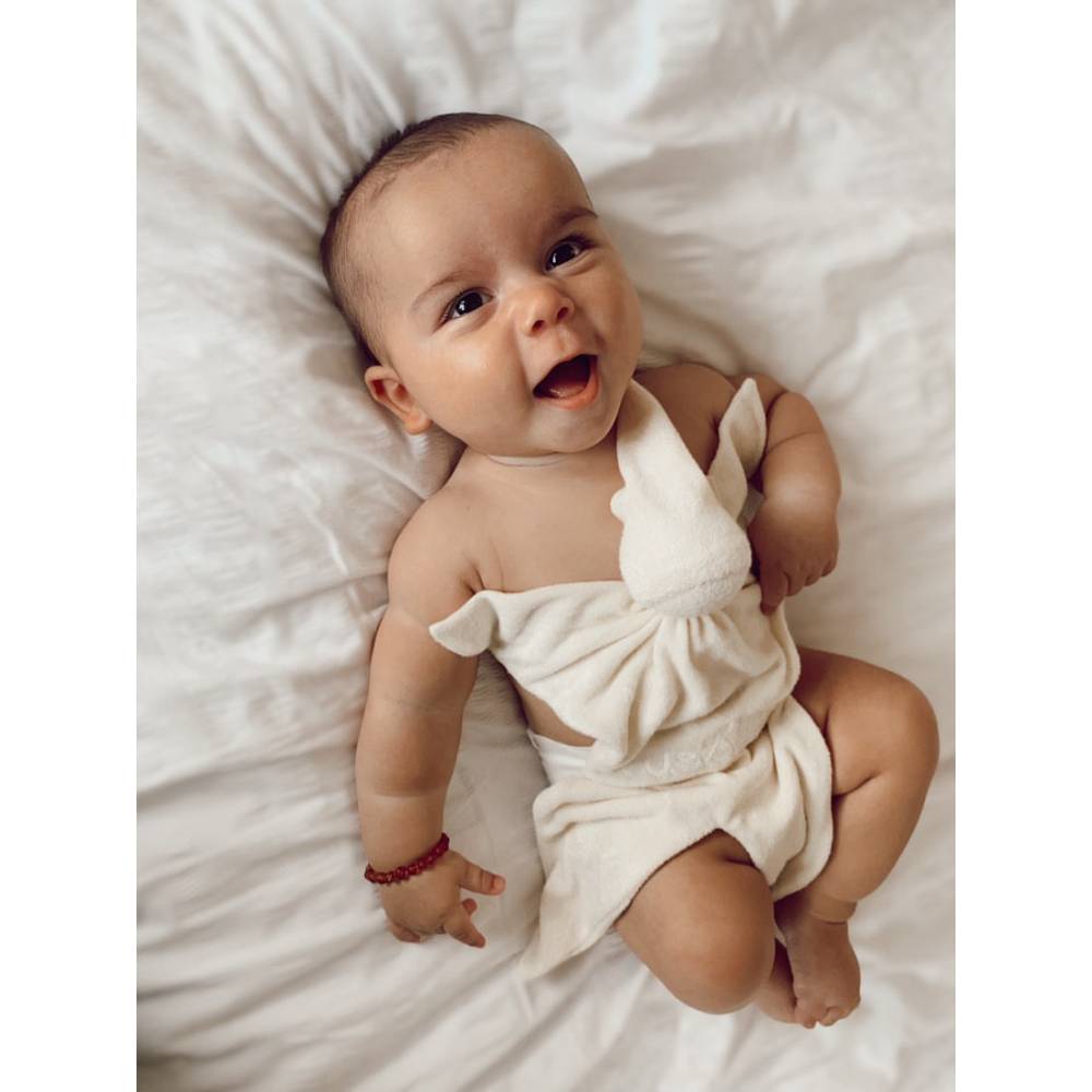 Infant in cot holding Cream Cuskiboo comforter