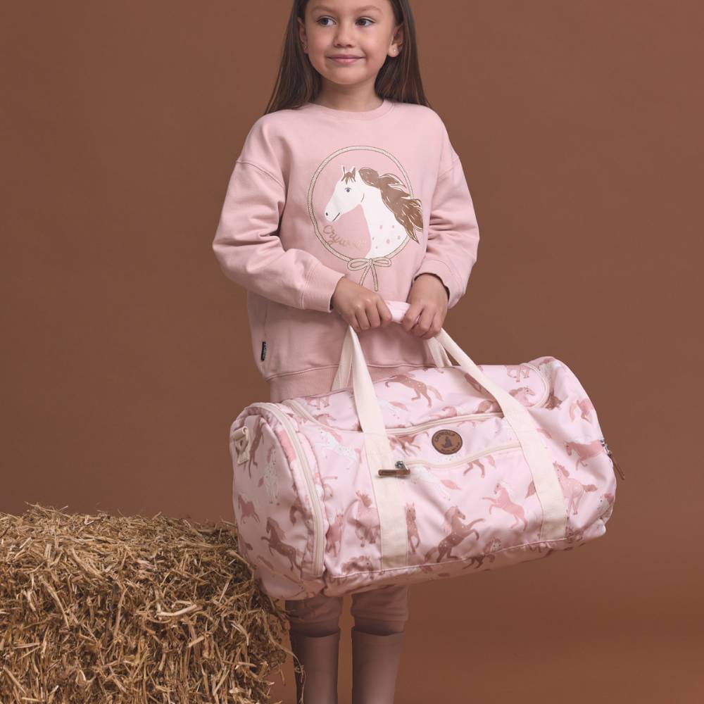 Young girl holding a pink duffel bag with horse design against a brown background