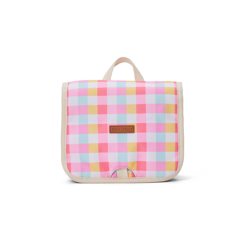 A small square toiletry bag with a pastel pink, yellow, and light blue gingham pattern, featuring a beige handle and trim, and a small brown leather brand patch that reads 'CRYWOLF'.