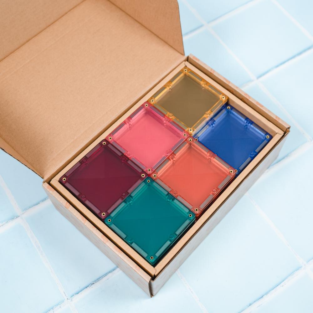 Set of colorful transparent square blocks in a cardboard box on a tiled floor.
