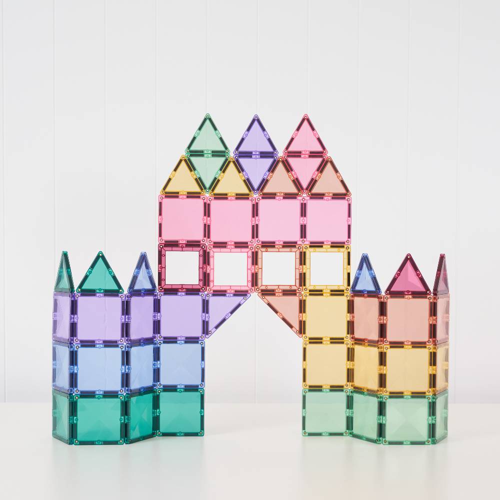 A set of translucent magnetic building tiles arranged to form a castle-like structure with towers and an archway, photographed on a clean white surface against a white paneled background.