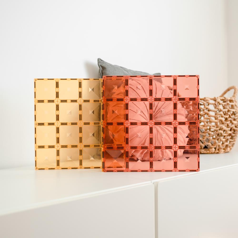 Two transparent geometric containers, one yellow and one pink, on a white surface with a neutral background.