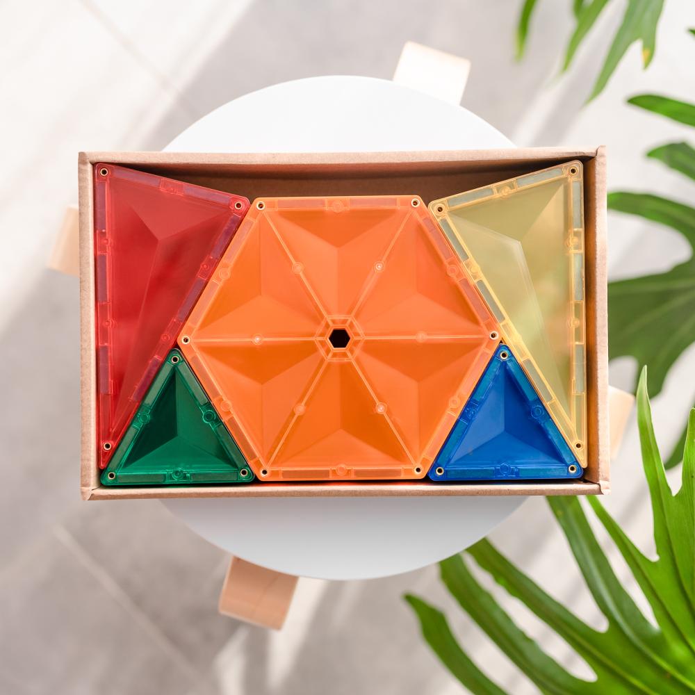 Colorful Connectix geometric building blocks in a wooden box with green leaves in the background