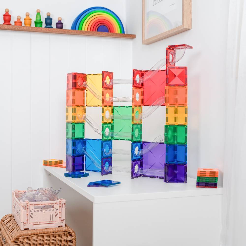 Colorful magnetic building blocks on a white surface with a rainbow toy in the background.