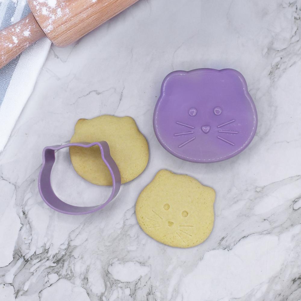 Purple cat-shaped cookie cutter with two shaped cookies on a marble surface.