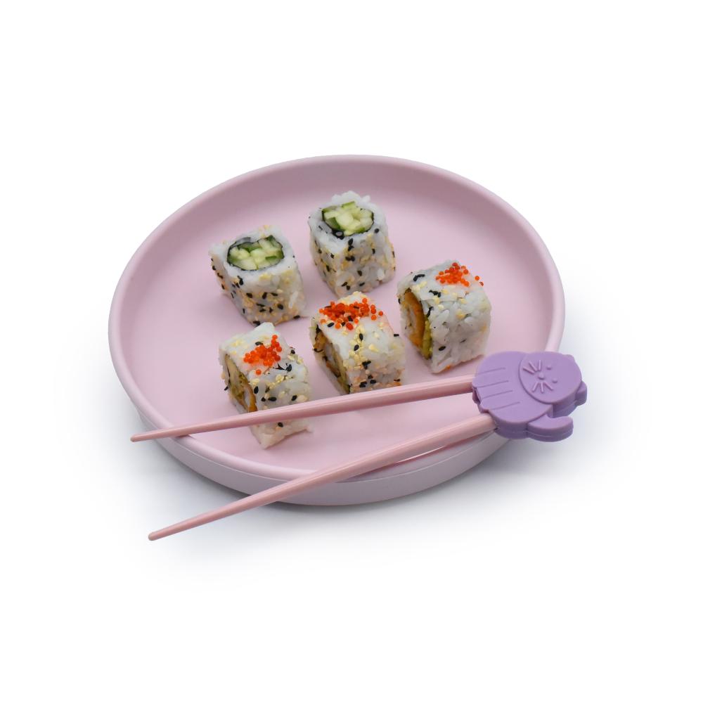 Pink plate with sushi rolls and purple chopstick trainer  on a white background