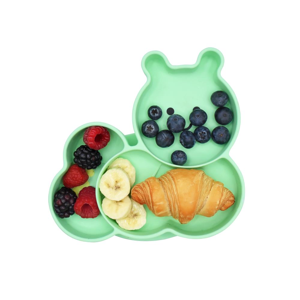 Green children's snack plate with berries, bananas, and a croissant on a white background