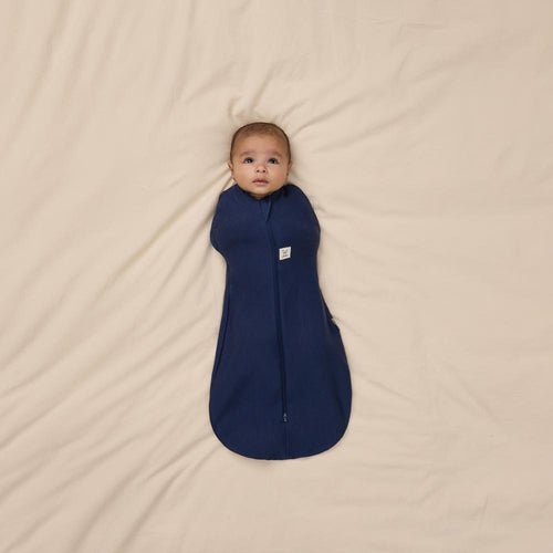 Baby wrapped in a blue swaddle on a beige blanket