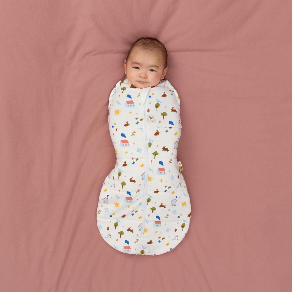Baby wrapped in a colorful patterned swaddle on a pink blanket