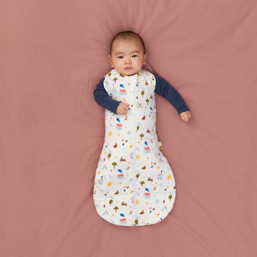 Baby lying on a pink blanket wearing a patterned sleep bag.
