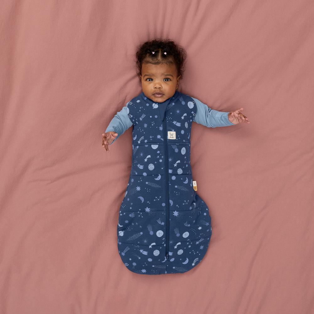 Baby lying on a pink blanket wearing a blue sleeping bag with space pattern