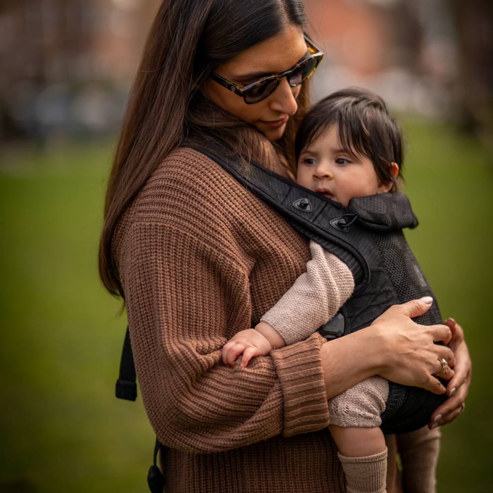 Woman holding a child in a black magnetic buckle Carifit carrier outdoors