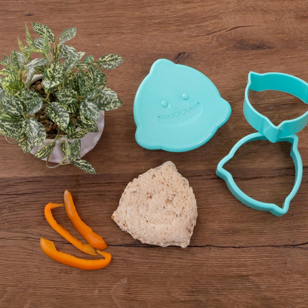 Teal lemon-shaped cookie cutter with a piece of lemon and orange peel on a wooden surface.