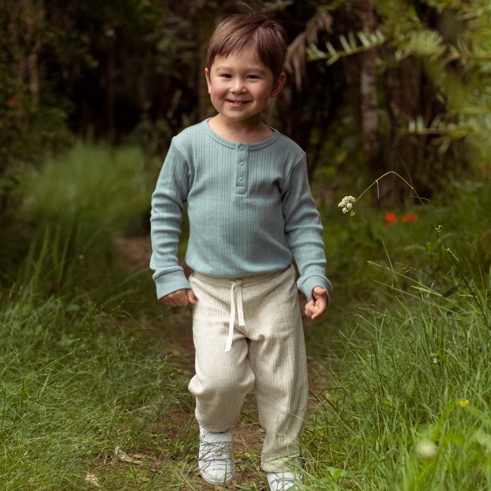 Child wearing a light blue sweater and beige pants standing in a grassy field.