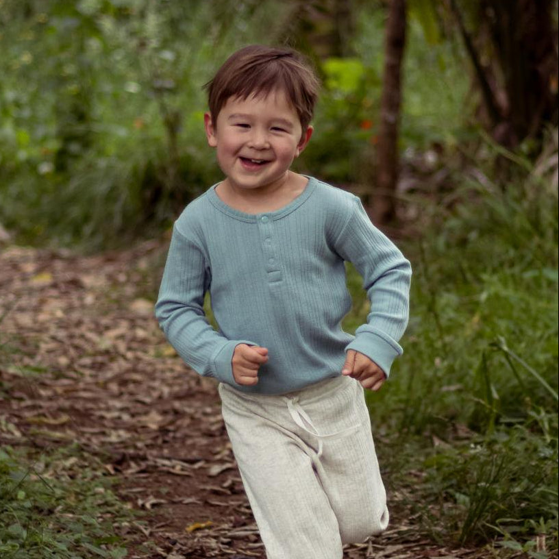 Child running on a dirt path in a natural setting wearing a woolbabe light teal top