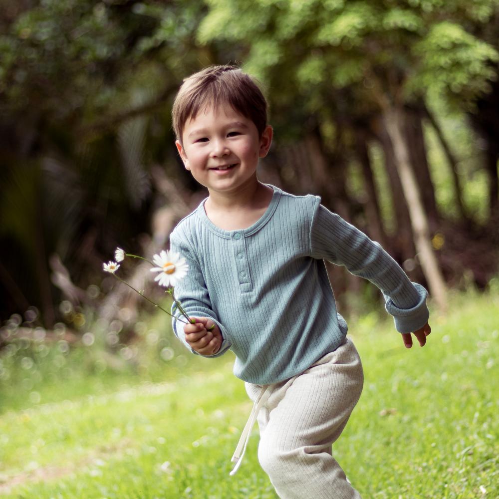 Child in a blue shirt holding a flower in a grassy outdoor setting