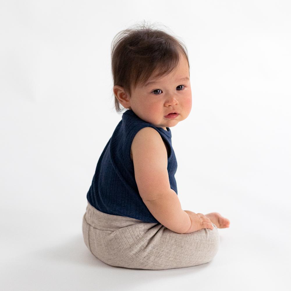 Baby wearing a blue sleeveless top and beige pants on a white background
