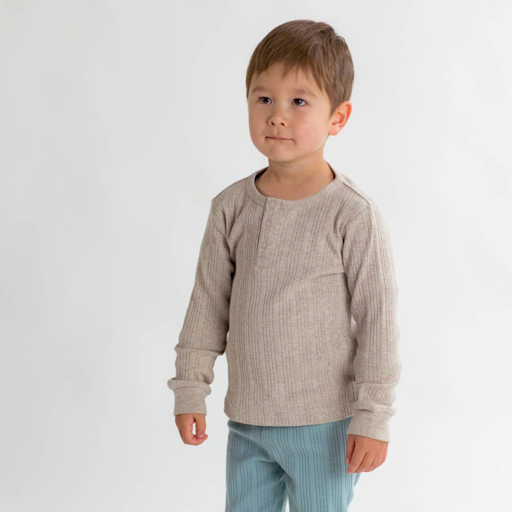 Young boy wearing a beige long-sleeve shirt and light blue pants on a white background