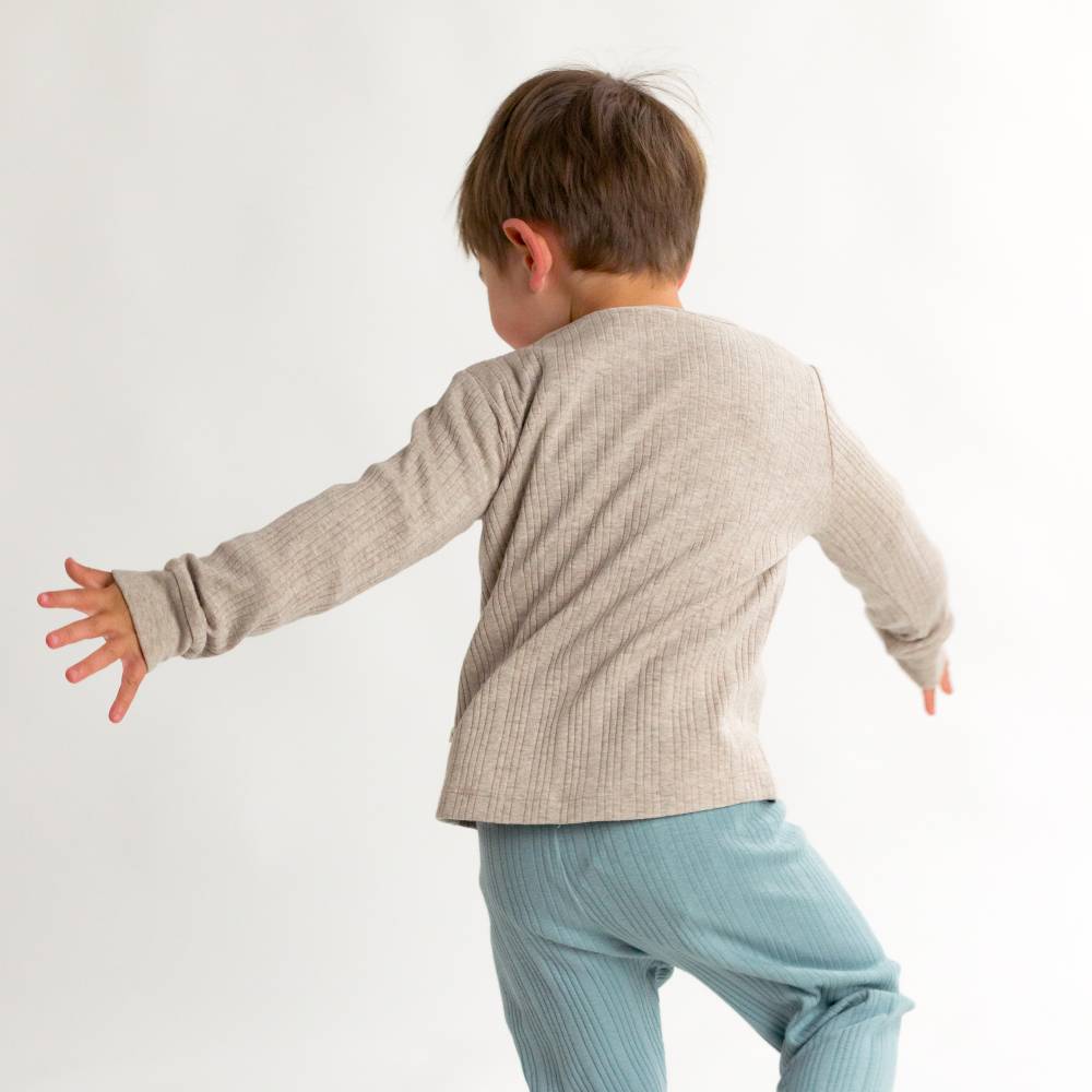 Child wearing a beige long-sleeve shirt and light blue pants on a white background