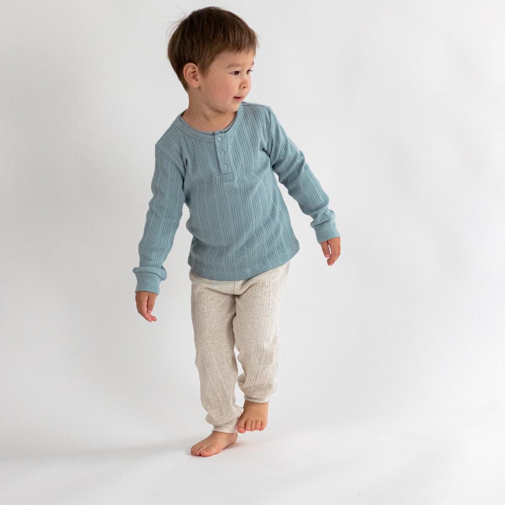 Child wearing a blue long-sleeve shirt and beige pants on a white background