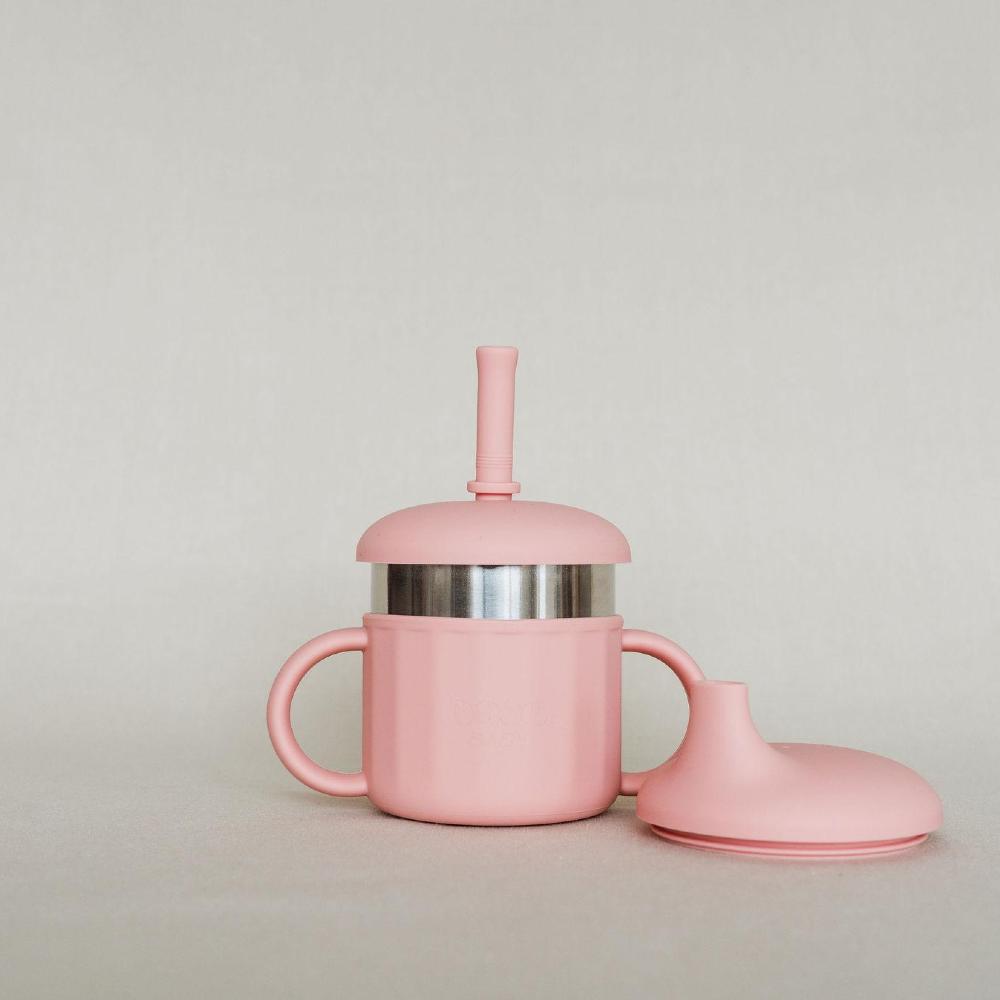 A pink silicone baby cup with a stainless steel inner liner, a matching pink straw lid, and a separate pink silicone spout lid, set against a neutral light gray background.