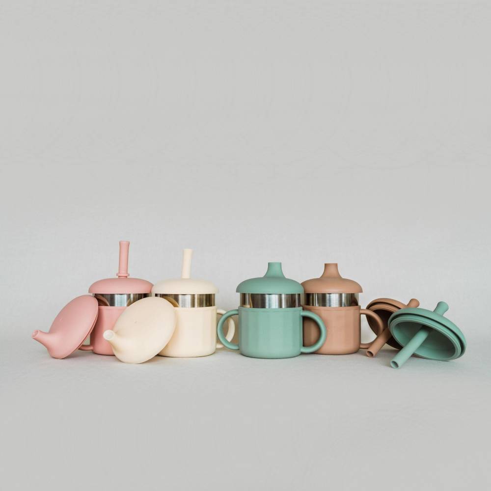 A set of pastel-colored silicone baby sippy cups and lids with stainless steel bands, arranged on a light gray background.